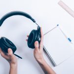 Female hands hold headphones at the desk with a notepad and pen